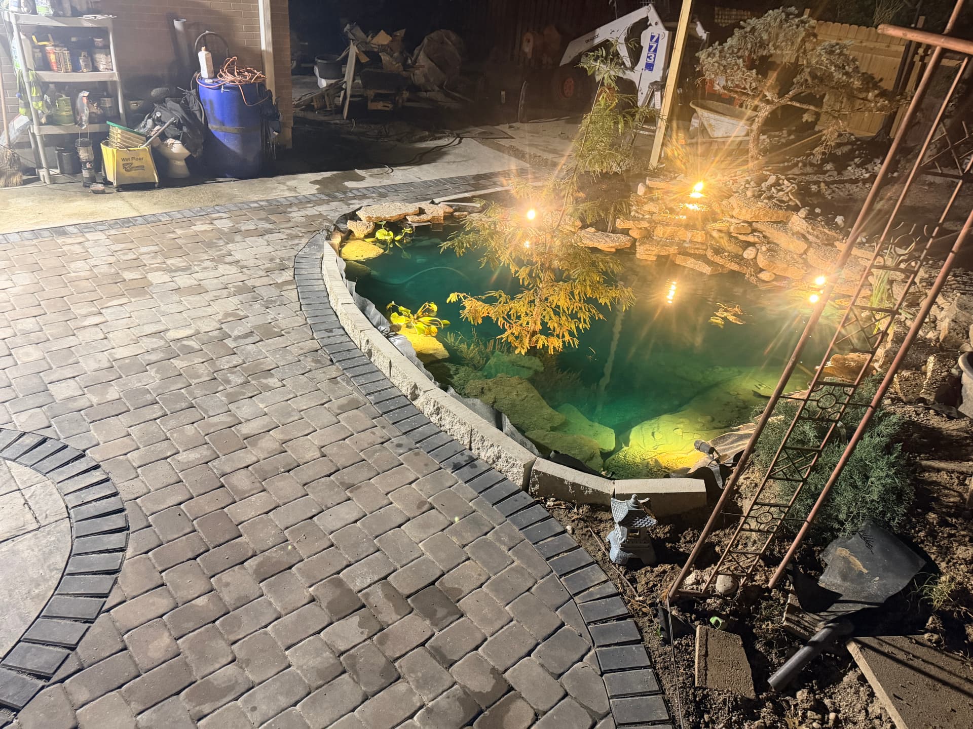 Herringbone paver patio with a lit koi pond and waterfall at night in Oxford, Ohio